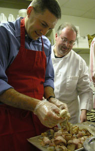 Steve Eiting, complete with hair net, gets a little instruction from Chef Matt Baker on how to place bacon-wrapped scallops onto skewers during a cooking class Saturday night at Haus der Eleganz in Minster. After three hours of the cooking class, Eiting and four other men served an elegant meal to their wives as a Valentine's Day gift.&nbsp;&nbsp;<br></br>dailystandard.com